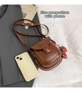 Brown vintage saddle bag with strawberry charm shown next to a phone for size comparison
