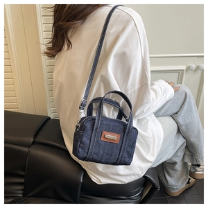Close-up of denim mini handbag with white stitching and leather patch on model