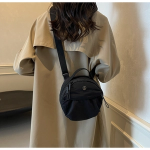 Detail of high-quality black nylon crossbody bag worn with a beige trench coat