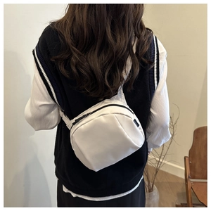Rear view of model wearing a minimalist white canvas shell bag with black zipper detail