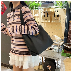 Close-up of a large black canvas tote bag with a brown leather label in a lifestyle setting