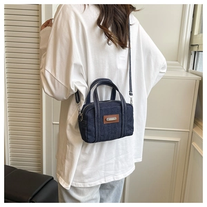 Detail of dark blue denim crossbody bag with white stitching and leather brand tag