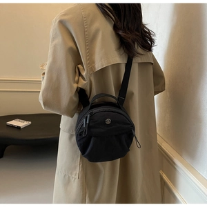 Detail of a black nylon crossbody round bag with dual zippers and a circular metal logo