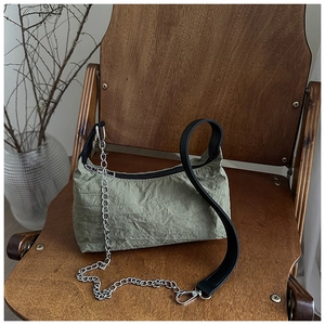 Detail of green ruched shoulder bag with black strap and silver chain on a wooden chair