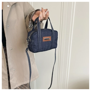 Detail of dark blue denim pillow bag featuring brown leather patch and metal accent
