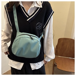 Detail of light blue nylon crossbody bag with zipper and adjustable strap on a model