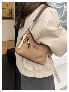 Detail of canvas shoulder bag with leather trim and decorative beaded tassel charm