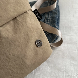 Minimalist beige nylon bucket bag with pleated texture and stylish metal emblem detail