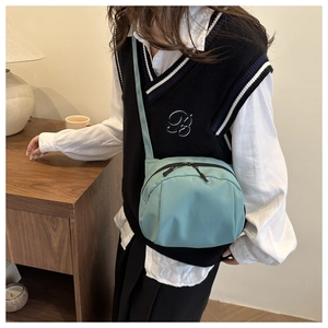 Detail of mint green nylon shell bag worn as a crossbody with double zip closure