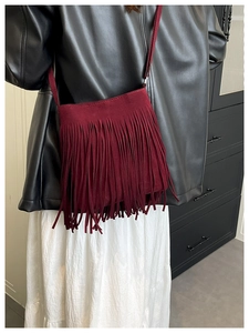 Detail of burgundy fringe crossbody bag with suede texture on a stylish fashion model
