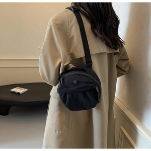 Close-up of a black nylon round crossbody bag featuring a metal M logo on a female model