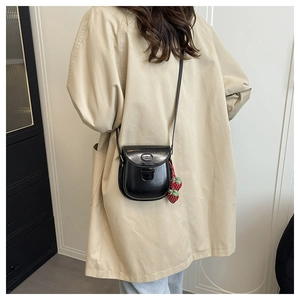 Détail d'un sac besace noir brillant avec breloques fraises sur un trench beige