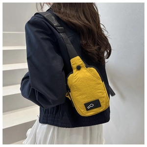 Outdoor shot of a yellow nylon crossbody bag featuring an adjustable black strap and logo