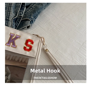 Close-up of golden hardware hook and towel embroidered letters on white leather bag