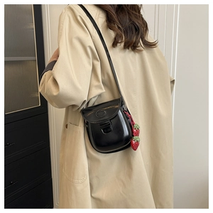 Detail of black glossy patent leather saddle bag with strawberry charm on a model