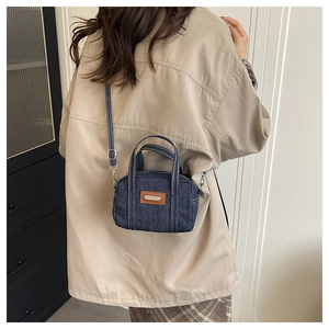 Detail showing the dark blue denim crossbody bag with vintage brown leather patch