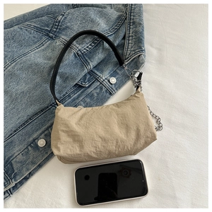 Detail of beige pleated shoulder bag with silver chain strap beside a smartphone