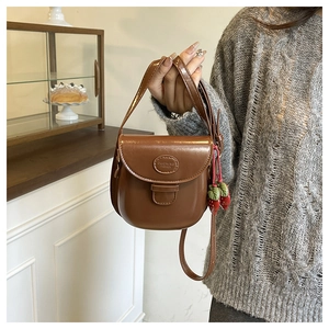 Close-up of caramel brown saddle bag with DUONING FASHION logo and strawberry charm