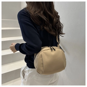 Detailed side view of beige crescent crossbody bag worn by model in minimalist setting