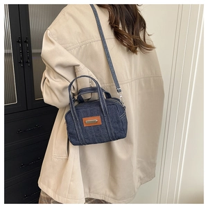 Detail of blue denim crossbody bag with white stitching and leather patch on model