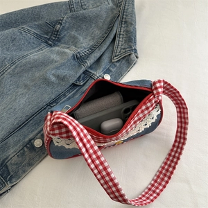 Denim shoulder bag with white lace trim and red gingham knotted straps on denim background