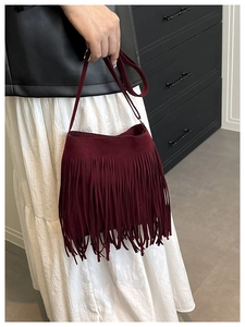 Detail view of burgundy fringed saddle bag showing soft suede texture and long tassels