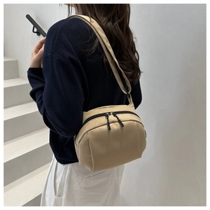 Close-up of a beige nylon crossbody bag with dual zippers worn by a model in casual style