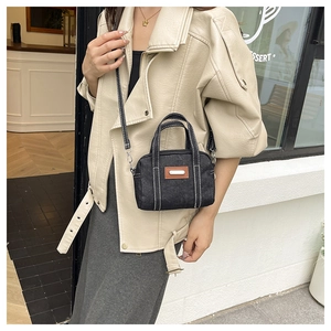 Detail of black denim handbag featuring brown leather patch and white contrast stitching