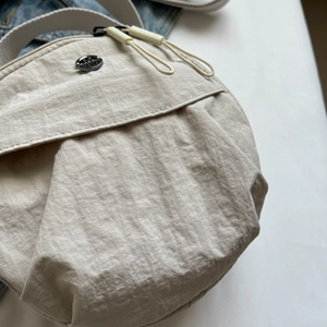 Chic beige round nylon crossbody bag with double zippers and stylish pleated finish