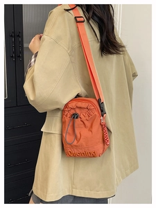 Detail of orange nylon crossbody bucket bag with drawstring closure and brand embroidery
