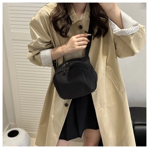 Modern black nylon shell crossbody bag shown styled with a casual trench coat and skirt