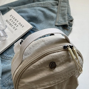 Modern beige nylon crossbody bag with round metal logo on denim jacket background
