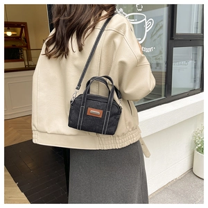 Detail of a denim crossbody bag with white contrast stitching and a vintage leather patch