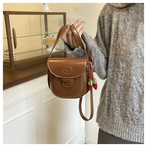Détail d'un sac besace marron vintage au fini brillant avec charme de fraise