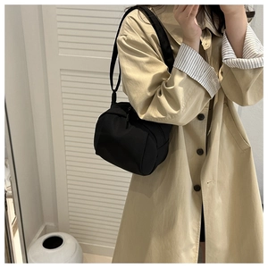 Minimalist black shell crossbody bag shown with a beige trench coat for a casual look