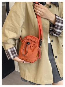 Detail of orange nylon crossbody bag featuring drawstring pocket and embroidery