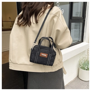 Detail view of a black denim pillow bag with white stitching and leather patch decoration