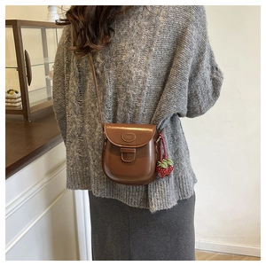 Detailed view of brown saddle crossbody bag with cute strawberry charm on knit sweater