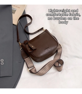 Detail of dark brown bucket bag with wide chevron strap and FASHION logo on white fabric