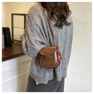 Détail du sac besace en cuir marron avec breloques fraises et logo embossé
