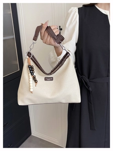 Détail d'un sac seau en toile beige avec garniture en cuir brun et gland perlé