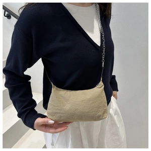 Detail view of a beige nylon crescent bag with silver chain strap and minimalist design