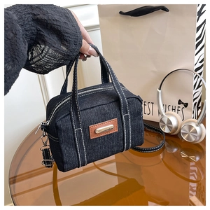 Detailed shot of dark blue denim pillow bag with white stitching and leather label