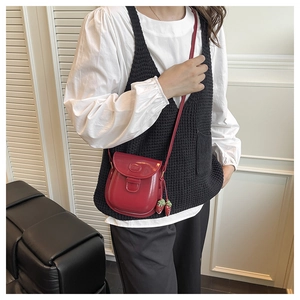 Détail d'un sac selle en cuir verni rouge avec breloques fraises décoratives