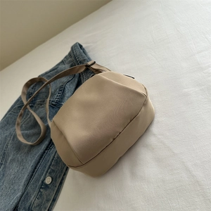 Minimalist khaki nylon shell-shaped crossbody bag on blue denim jacket background