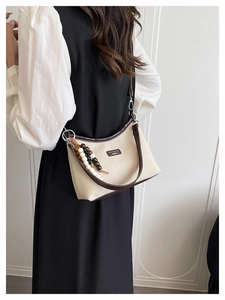 Detailed view of canvas shoulder bag with brown leather trim and beaded pendant detail