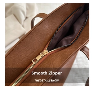 Macro shot of smooth gold zipper detail and pebble texture on brown leather tote bag