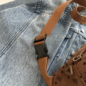 Brown corduroy crossbody bag with heart pattern and adjustable strap on denim background