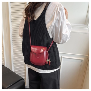 Detail of red leather saddle bag featuring a round logo and sweet strawberry charms