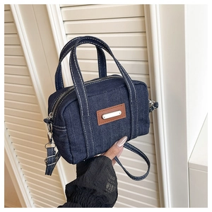 Detail of blue denim mini Boston bag featuring leather patch and adjustable shoulder strap